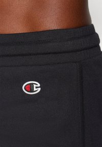 Sorte treningsshorts med elastisk midje og en liten, brodert logo med røde og hvite detaljer. Laget av mykt, pustende materiale.