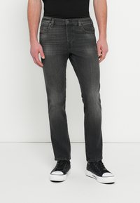 Tmavomodré džínsové nohavice s úzkym strihom, s prednými vreckami, vyblednutou textúrou a zapínaním na kovový gombík, kombinované s čiernymi teniskami.