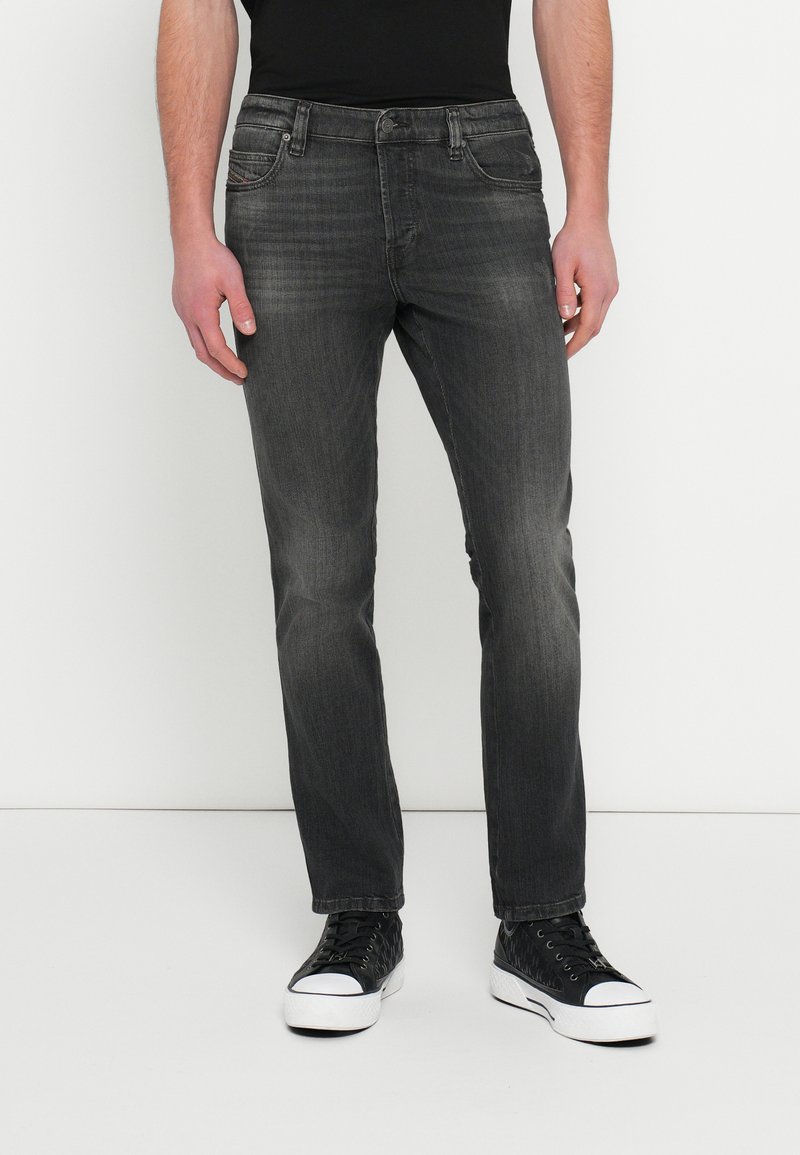 Tmavomodré džínsové nohavice s úzkym strihom, s prednými vreckami, vyblednutou textúrou a zapínaním na kovový gombík, kombinované s čiernymi teniskami.