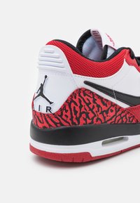 Czarna, biała i czerwona pięta sneakersów Air Jordan z czarnym logo Jumpman i czerwonym wzorem na białym tle.