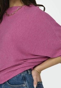 Top rosa a coste, dal taglio ampio, con maniche larghe e scollatura rotonda, abbinato a un jeans a vita alta, impreziosito da un bracciale in oro.