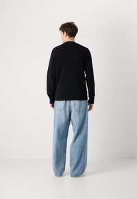 Zwarte gebreide trui met lange mouwen en ronde halslijn, gecombineerd met losse lichtblauwe denim jeans met achterzakken.