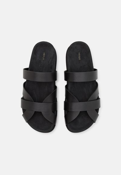 Sandales noires à semelle avec des lanières croisées en cuir lisse et une semelle intérieure douce et texturée. Design minimaliste sans matériel visible.
