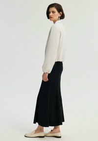 Kermakelt jacket, jossa on kootut hihansuut, musta kellotettu hame ja vaaleanbeige loafersit. Yksinkertainen muotoilu, sileä tekstuuri ja neutraalit värit.