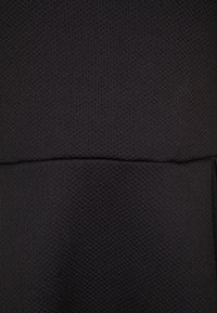 Tissu noir texturé avec un motif 3D subtil, présentant des coutures au niveau de la taille. Le matériau semble extensible et lisse.
