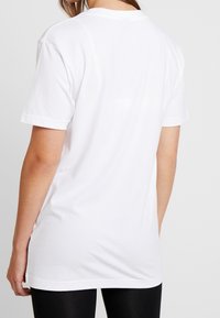 Bílý tričko s krátkými rukávy a kulatým výstřihem, vyrobené z jemné bavlny, s uvolněným střihem a kontinuální texturou na zádech.