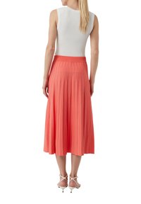 Koronkowa spódnica plisowana w kolorze koralowym z szerokim pasem oraz pionowymi białymi paskami, zestawiona z dopasowanym białym topem bez rękawów i białymi sandałkami na obcasie.