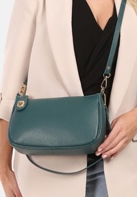 Teal leren schoudertas met een gladde textuur, rechthoekige vorm, gouden hardware accenten en een verstelbare schouderband.