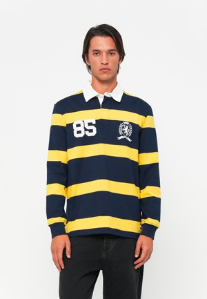 T-shirt de rugby à manches longues avec des rayures horizontales bleu marine et jaune, col blanc et blason brodé représentant un lion et le numéro 85.
