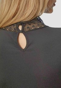Zwarte ribbeltop met een kanten kraag, details van een sleutelgat aan de achterkant met knopen en een gestructureerde afwerking.