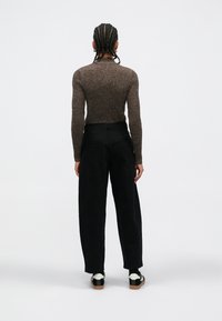 Top de punto marrón con textura acanalada, pantalones negros de pierna ancha y zapatos en negro y blanco, vistos desde atrás sobre un fondo blanco liso.