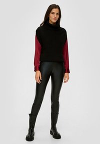 Pull à col roulé noir à côtes sur une chemise à manches longues bordeaux, associé à un legging en simili cuir noir et des bottes noires à semelle épaisse.