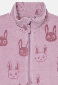Fleece zip-up jakke i lys rosa, med opphøyet krage og et heltrykt kaninmønster i mørkere nyanser av rosa. Myk tekstur.