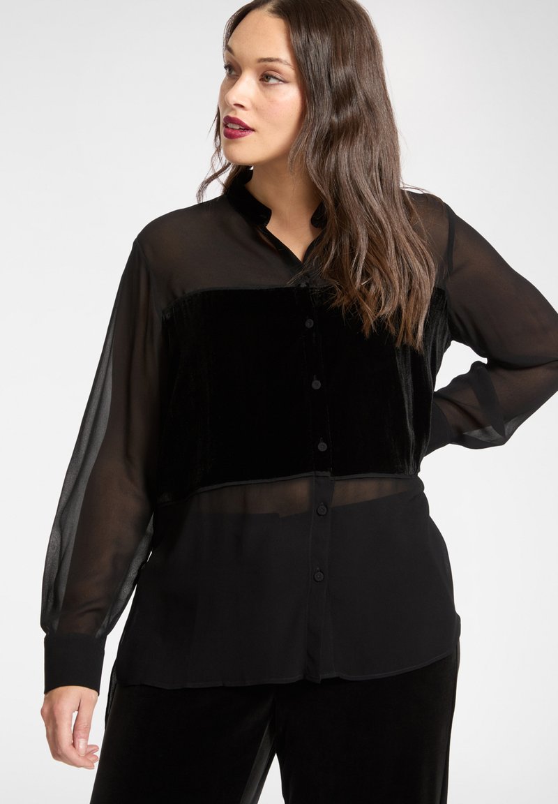 Czarna bluzka z przezroczystej tkaniny z aksamitną górną częścią, długimi rękawami, kołnierzykiem i zapięciem na guziki z przodu. Gładka faktura.
