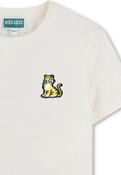 T-shirt in cotone crema con piccolo ricamo di una tigre gialla e nera sulla parte sinistra del petto. Collo girocollo classico e maniche corte.