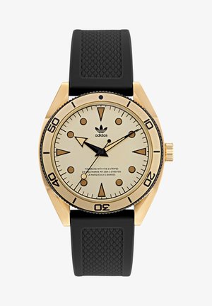 Orologio dorato con quadrante rotondo, cinturino crema, indici neri, e cinturino in gomma con superficie testurizzata e un logo alle 12.