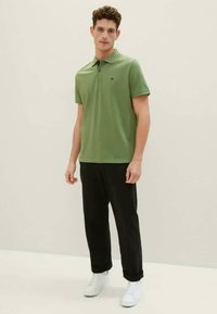 Πράσινο πόλο μπλουζάκι από βαμβάκι, με κλασικό γιακά και κοντά μανίκια. Συνδυάζεται με μαύρα παντελόνια και λευκά αθλητικά παπούτσια.