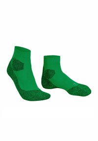 Un paio di calzini atletici verde a taglio basso con tacco e punta imbottiti di un verde più scuro su sfondo bianco.