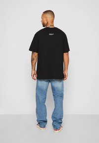 T-shirt preta de algodão com mangas curtas, um corte descontraído e uma pequena impressão de logotipo nas costas. Combinado com jeans de ganga azul claro.