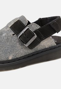 Sandal din suede gri, cu o curea neagră și o cataramă metalică, talpă din cauciuc și suprafață superioară texturată. Potrivit pentru uz casual.