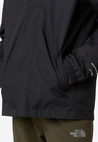 Schwarze wasserdichte Jacke mit elastischen Bündchen, Seitentaschen und einer strukturierten Oberfläche. Mit Logodetails am Ärmel und im Kragenbereich.