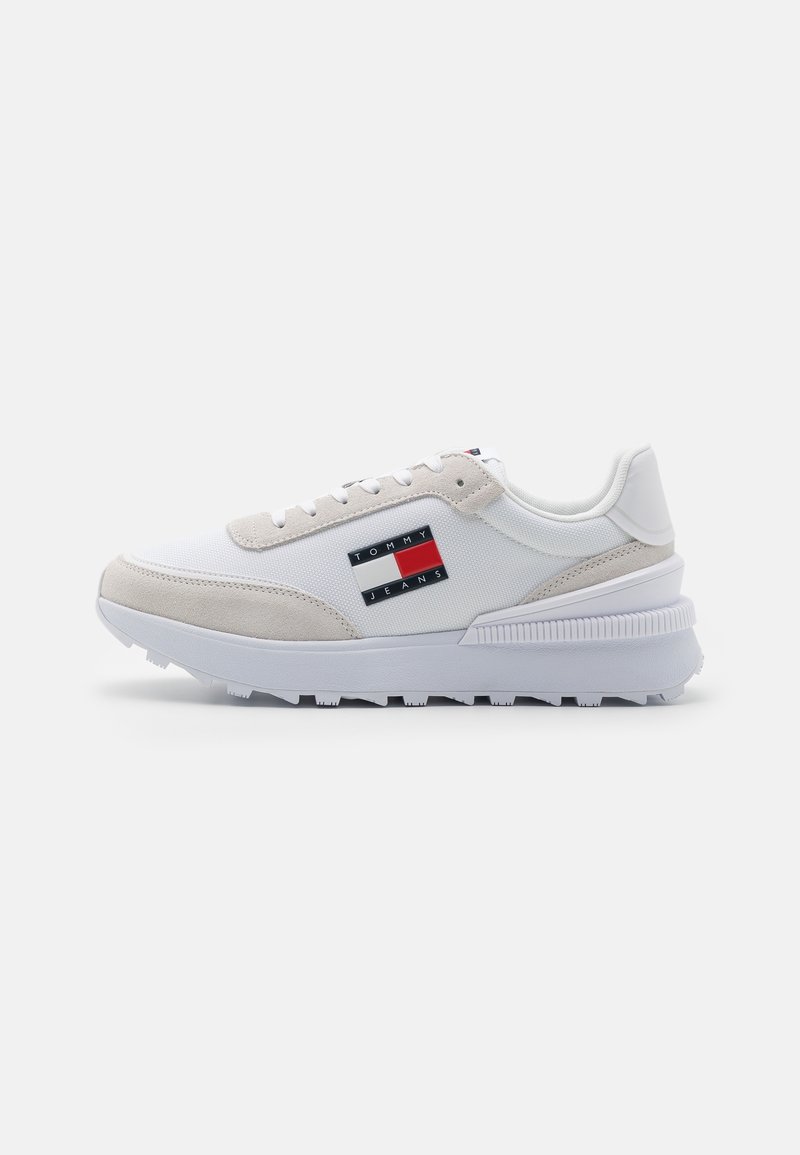 Vit sneaker med mockadetaljer, som har ett övre i tyg och en mönstrad sula. Visar en Tommy Jeans-logotyp i röd, vit och blå.