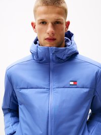 Helesinine puffjakki kõrge kraega, millel on vasakul rinnal väike Tommy Jeans logo ja lukuga eesmine sulgemine.