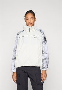 Lightweight, cream jacket with a high collar, featuring gray marble-patterned sleeves and a zip closure. Logo on chest and cuffs.