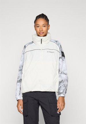 Lichte, crèmekleurige jacket met een hoge kraag, voorzien van grijs marmerpatroon op de mouwen en een ritssluiting. Logo op de borst en manchetten.