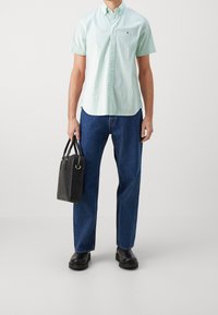 Camisa de manga corta verde claro con cuello abotonado, combinada con jeans de mezclilla azul y un bolso negro texturizado. Unos zapatos negros completan el look.
