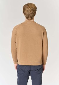 Felpa marrone con scollo e polsini a coste, caratterizzata da una trama semplice e un piccolo logo stampato vicino al collo posteriore, mostrata con pantaloni blu navy.