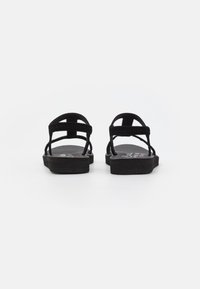 Sorte svarte sandaler har en flat såle, flere stoffremmer for støtte og et enkelt design med en teksturert overflate.