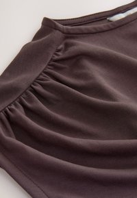 Mascarilla de tela marrón oscuro con pliegues recogidos y bordes cosidos, diseñada para ajustarse perfectamente sobre la nariz y la boca.