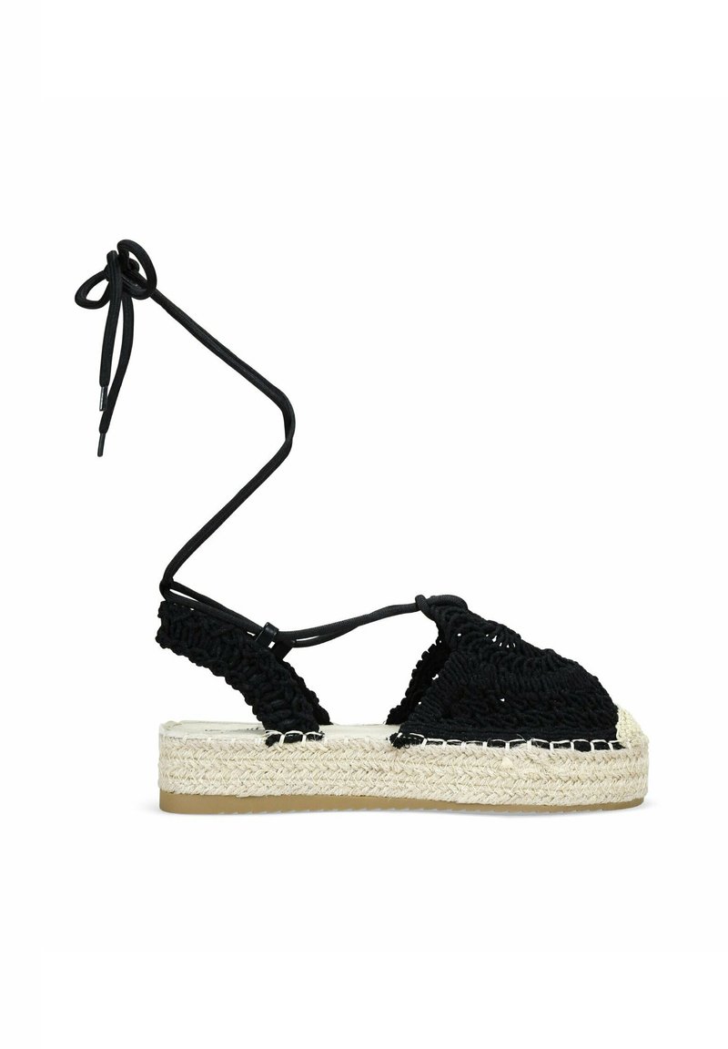 Espadrilles de crochet negro con lazos en el tobillo, con una suela intermedia de yute tejido y suela de goma, que destacan por su parte superior texturizada y diseño plano de plataforma.