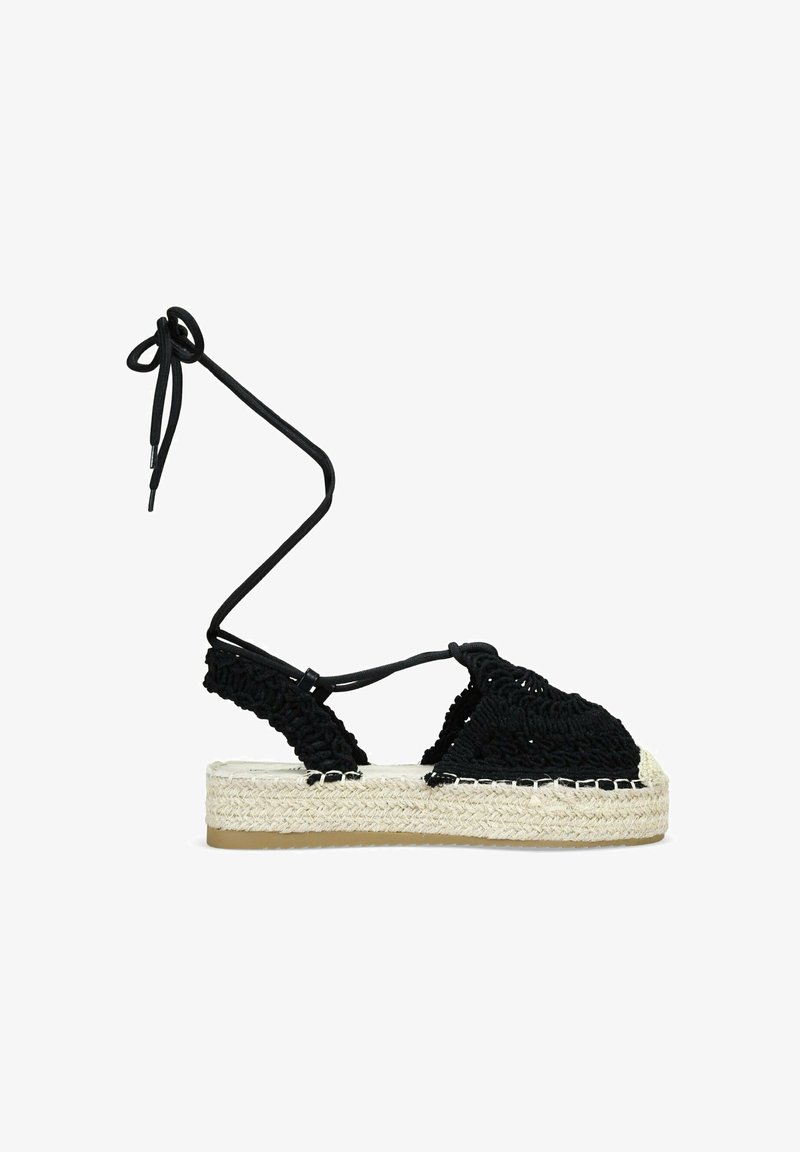 Espadrilles de crochet negro con lazos en el tobillo, con una suela intermedia de yute tejido y suela de goma, que destacan por su parte superior texturizada y diseño plano de plataforma.