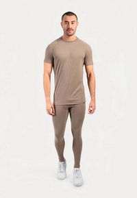 Tan korte mouw sportshirt gecombineerd met bijpassende legging. Soepel, elastisch materiaal; minimalistisch ontwerp; witte sneakers maken de outfit compleet.