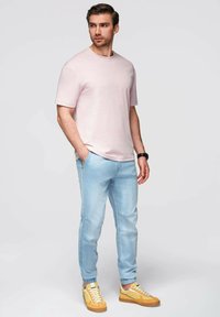 Světle růžové tričko s krátkým rukávem v kombinaci se světle modrými džíny a žlutými teniskami s bílými akcenty. Jednoduchý a ležérní design, přiléhavý střih.