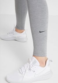 Szare legginsy z czarnym logo Nike i białymi butami sportowymi z szarymi akcentami i sznurówkami. Gładki materiał z dopasowanym krojem.