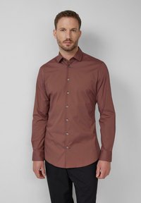 Roestrode blouse met lange mouwen en knoopsluiting, met een getailleerde pasvorm, voorzien van een gespreide kraag en glanzende knoopaccenten tegen een effen achtergrond.