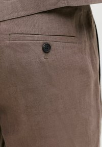 Εκτός πλάνου καφέ λινό παντελόνι με πίσω τσέπη που διαθέτει μαύρο κουμπί και διακριτή υφή.