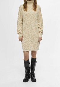 Beige pletené šaty s vysokým límcem, které mají jemný vzor zvířecího potisku a vypufované rukávy. Doplněné černými koženými botami do kolen.