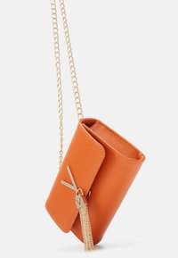 Orange texturerad läderväska med en guldkedjestraps, med ett klafflock och en dekorativ tofs med en bokstavshänge.