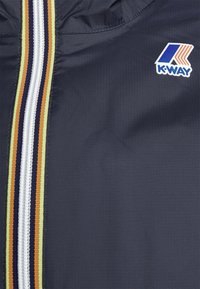 Fermeture éclair de veste bleu marine foncé avec des rayures bleu marine, blanches, orange et jaunes et un patch logo K-Way sur la poitrine.