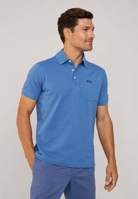 Niebieska koszulka polo wykonana z bawełny, z trzema guzikami na stójce, kieszenią na lewej piersi oraz krótkimi rękawami. Gładka tekstura.