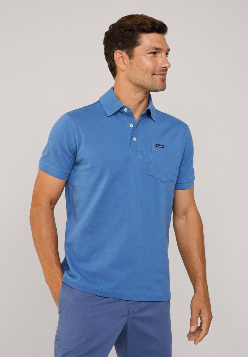 Niebieska koszulka polo wykonana z bawełny, z trzema guzikami na stójce, kieszenią na lewej piersi oraz krótkimi rękawami. Gładka tekstura.
