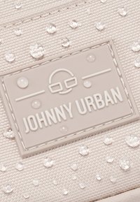 Világosszürke textília vízcseppekkel; emelt, téglalap alakú logóval rendelkezik, amelyen "JOHNNY URBAN" felirat és minimális design látható. Texturált felület.