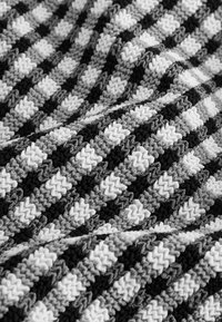 Gewebter Stoff mit Zickzackmuster in Schwarz, Weiß und Grautönen. Dicke Textur mit abwechselnden Streifen, die Tiefe erzeugen.