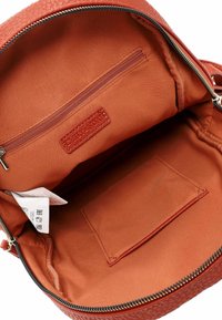 Brauner, strukturierter Innenraum eines Rucksacks mit glattem orangem Futter, ausgestattet mit einer Reißverschlusstasche und einer kleinen offenen Tasche zur Organisation.