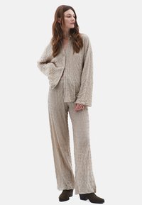 Beige lounge set met textuur, bestaande uit een button-up top en wijde broek, met een gekreukt stofafwerking en een losse pasvorm.