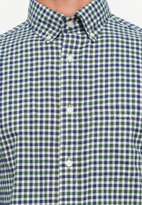 Korte mouwen overhemd met knopen in groen, blauw en witte geruite stof. Heeft een kraag, een voorzak en het merkembleem aan de zijkant.